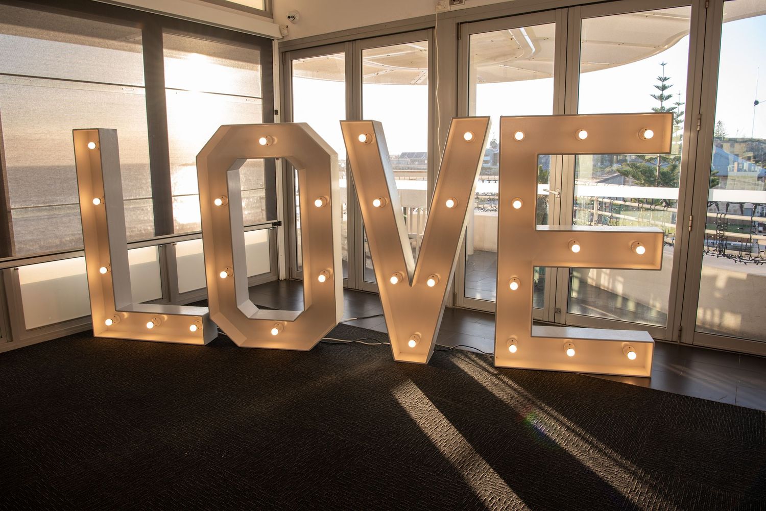 Large illuminated LOVE marquee letters displayed in a modern space with glass windows and natural lighting.