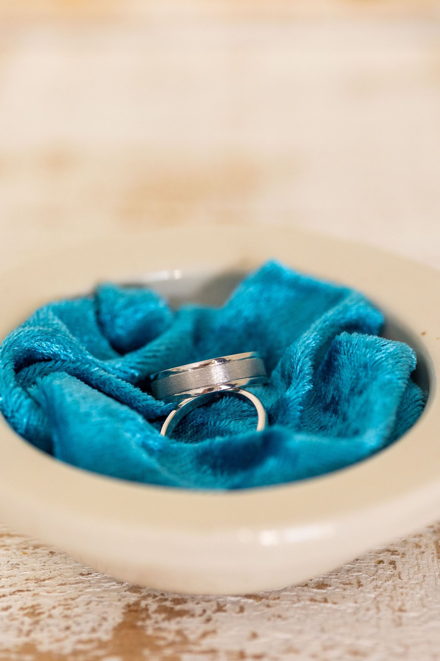 Wedding rings nestled on a plush turquoise blue velvet fabric in a white ceramic dish.
