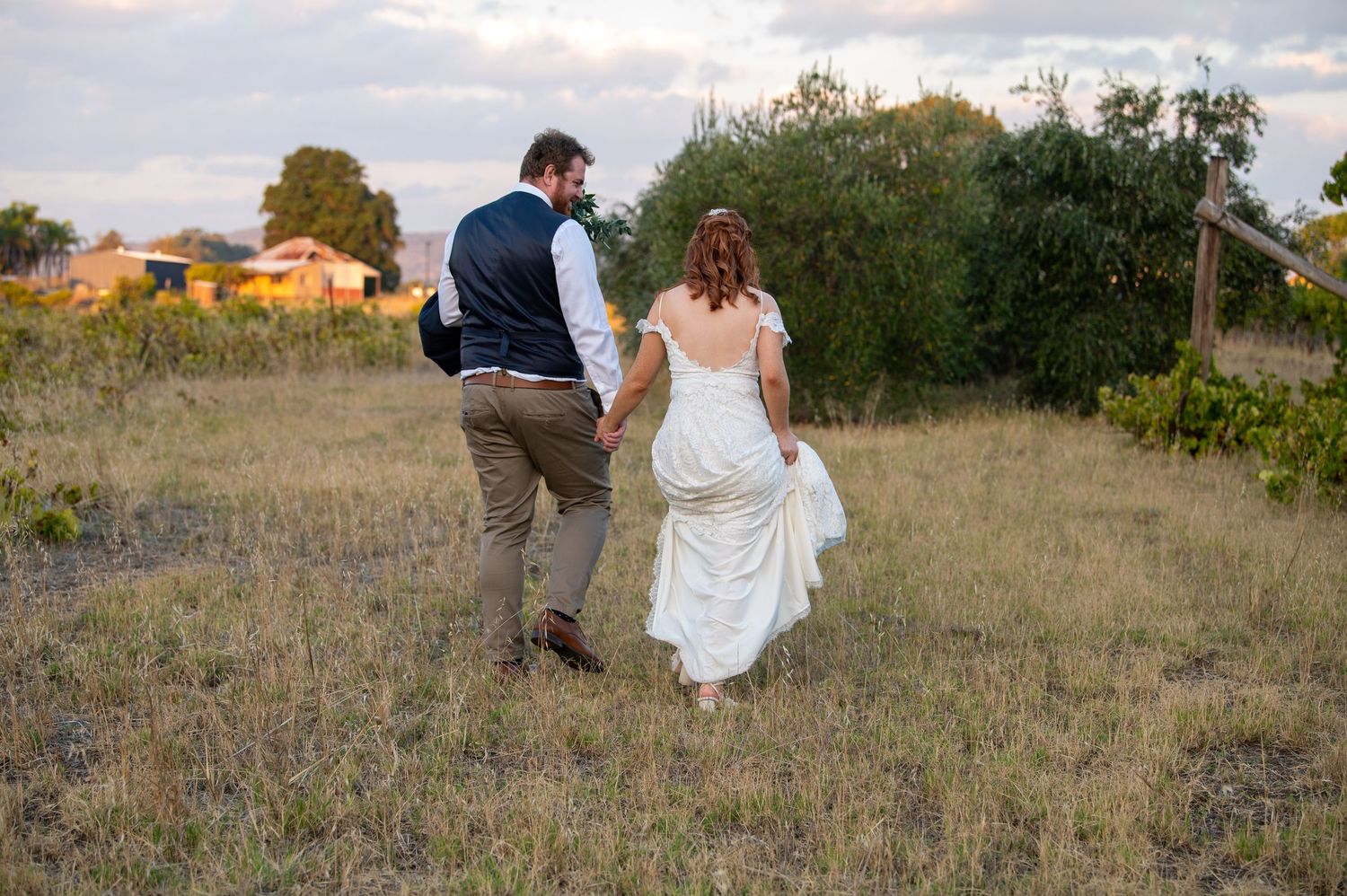 Newlyweds share intimate moment while sitting together on hillside during sunset.