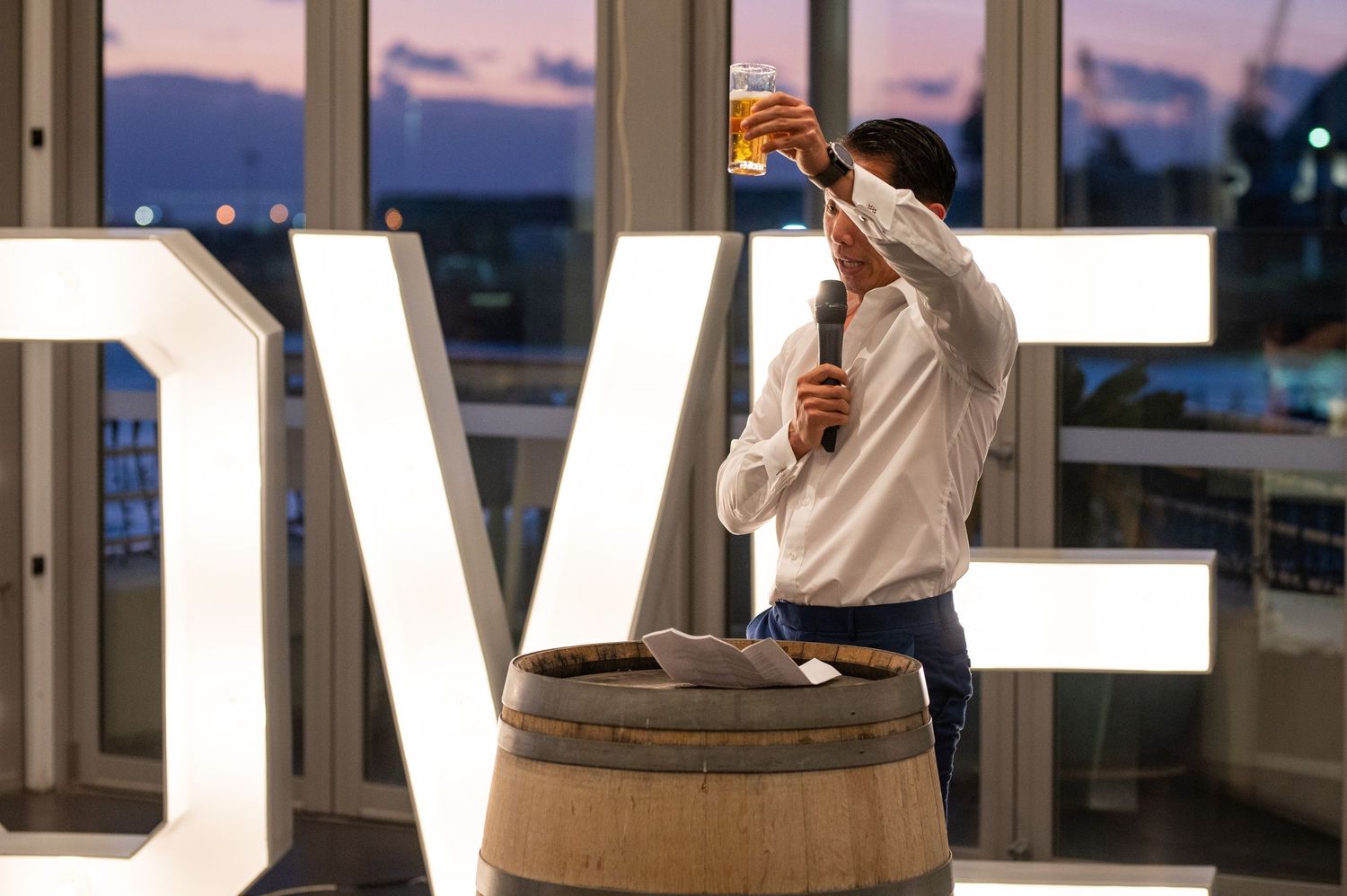 Person pouring drinks at a barrel station with illuminated letter decor at a wedding reception.