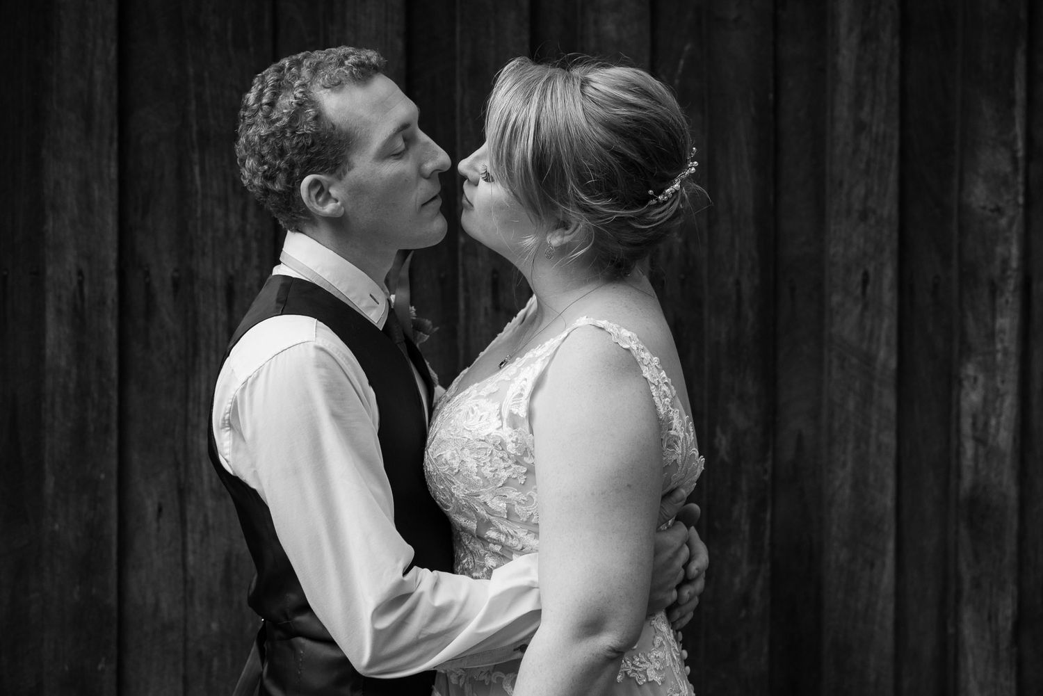 A romantic black and white photo of a newlywed couple sharing an intimate moment against a wooden wall background.