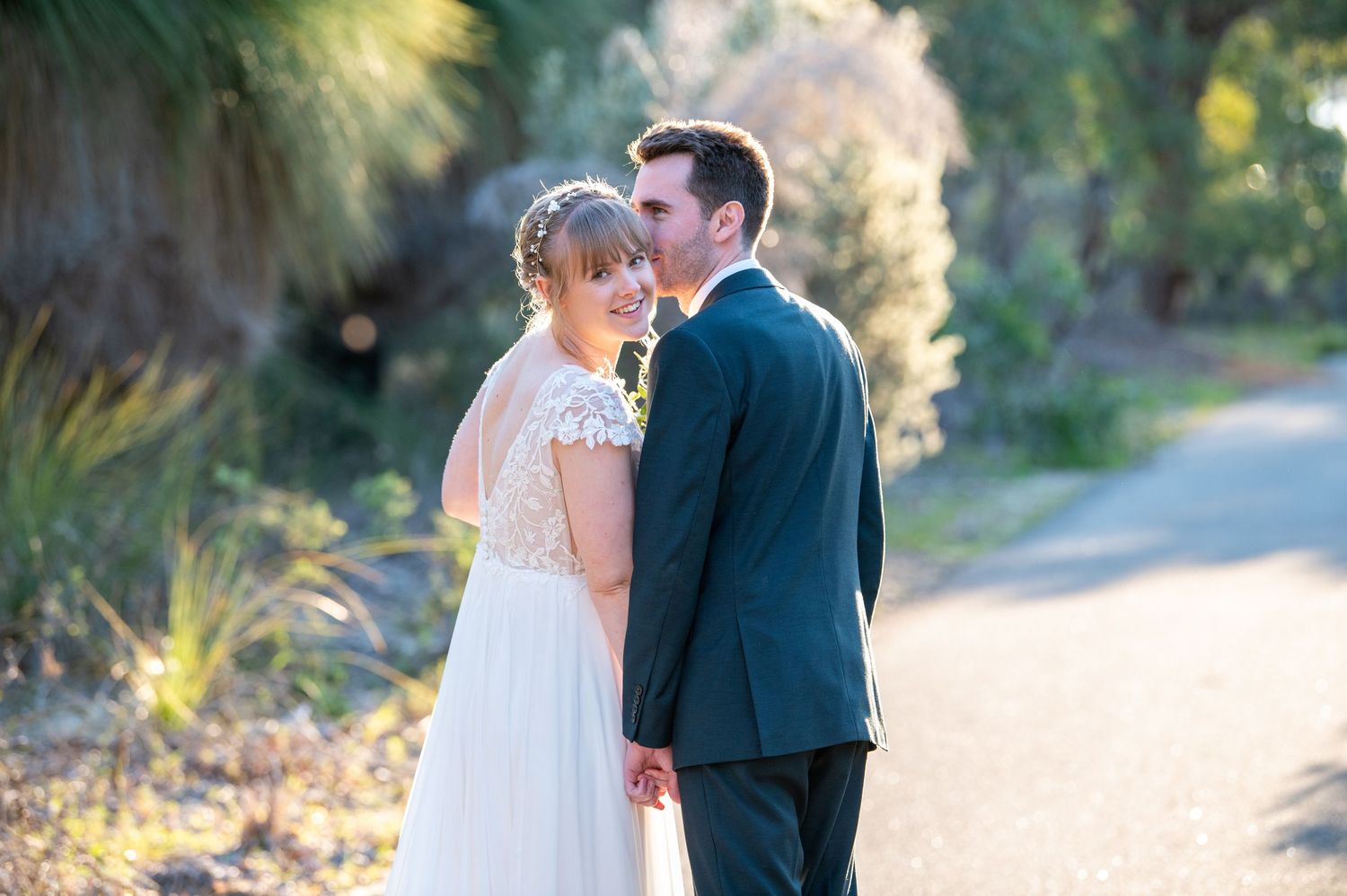 Romantic outdoor wedding couple portraits captured on a tree-lined path during sunset.