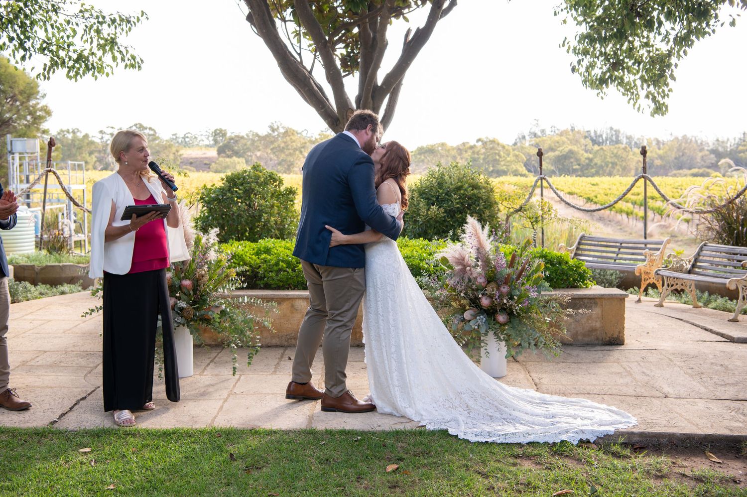 An intimate outdoor wedding ceremony taking place under a tree with floral decorations.
