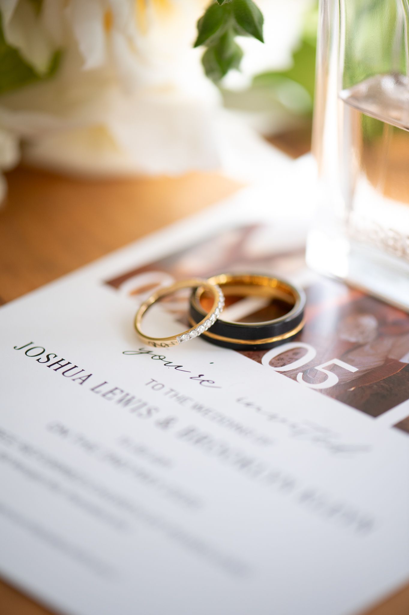 Wedding rings rest on marriage documents with scattered floral decor and warm lighting creating a romantic detail shot.