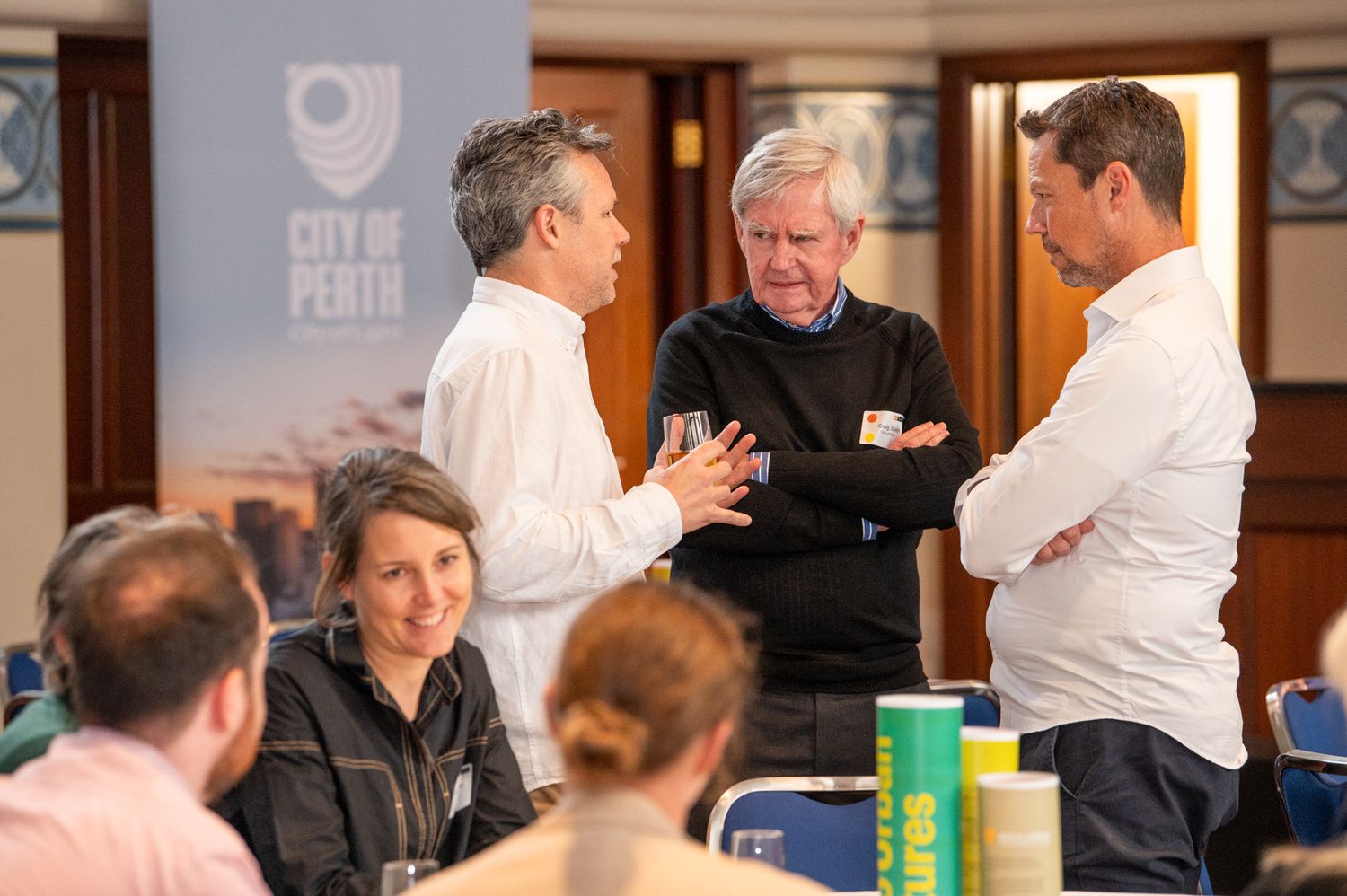 A group of people have a lively discussion during a business meeting with the Open University logo visible in the background.