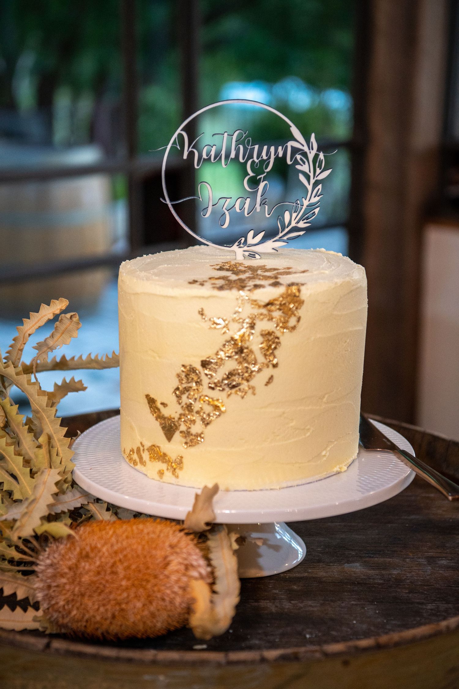 An elegant white wedding cake with gold accents and a clear acrylic topper.