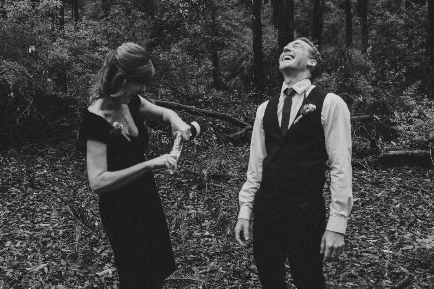 A joyful black and white photo captures two people sharing a candid laughing moment outdoors in formal attire.