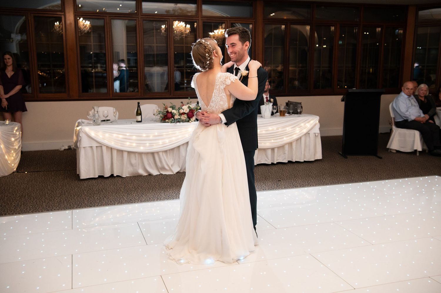 Couple sharing their first dance in an elegant reception hall with decorated white tables.