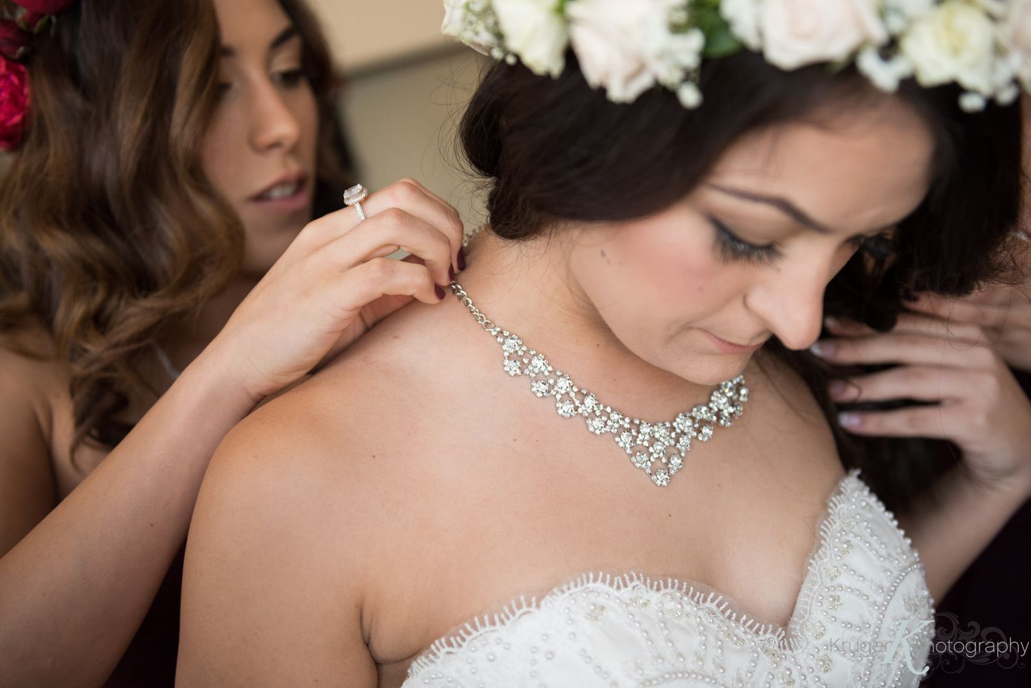 Sparkly crystal necklace being fastened on bride wearing strapless white wedding dress and flower crown