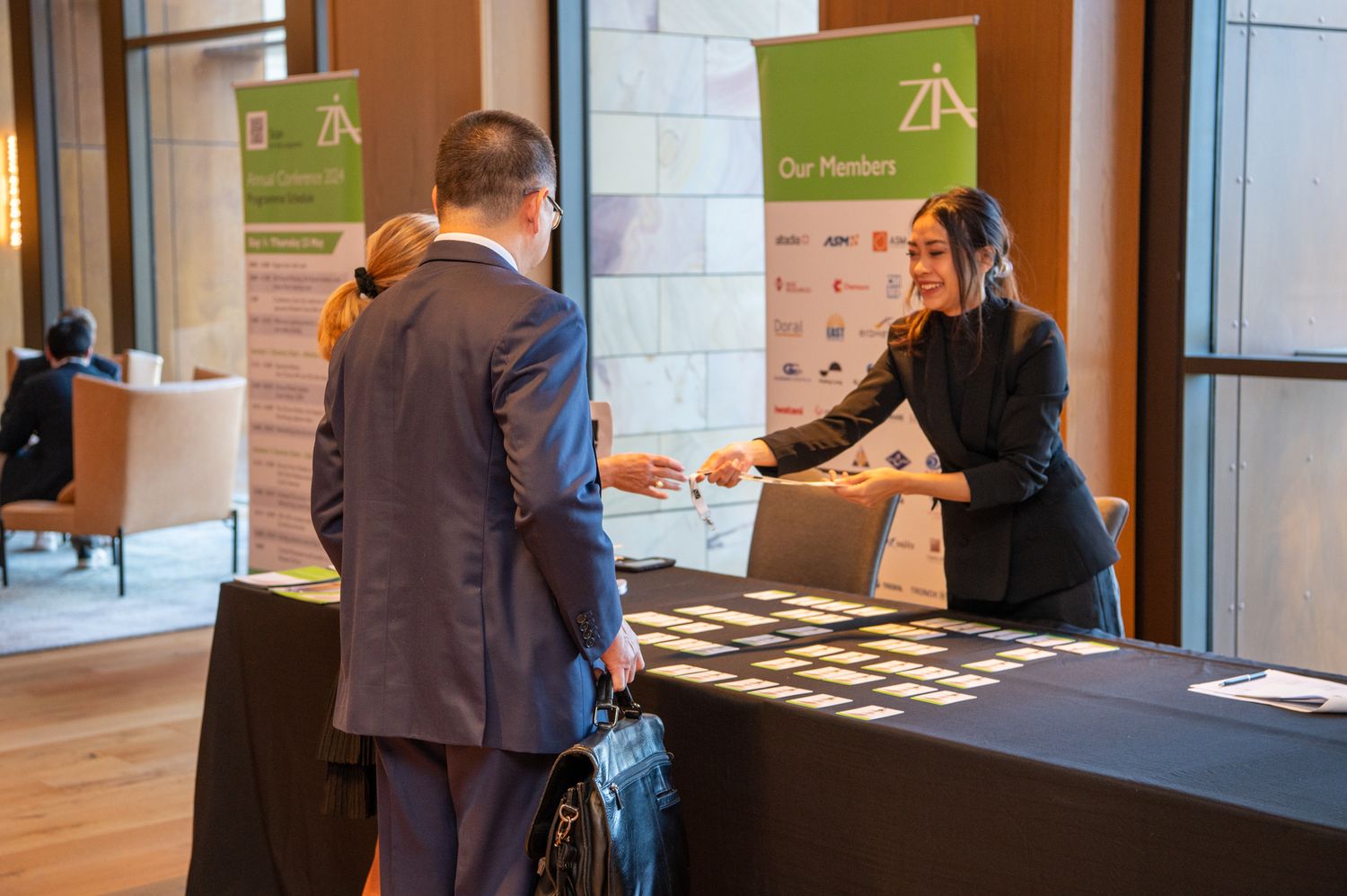 A professional interaction between two individuals at a business reception desk with a black tablecloth.