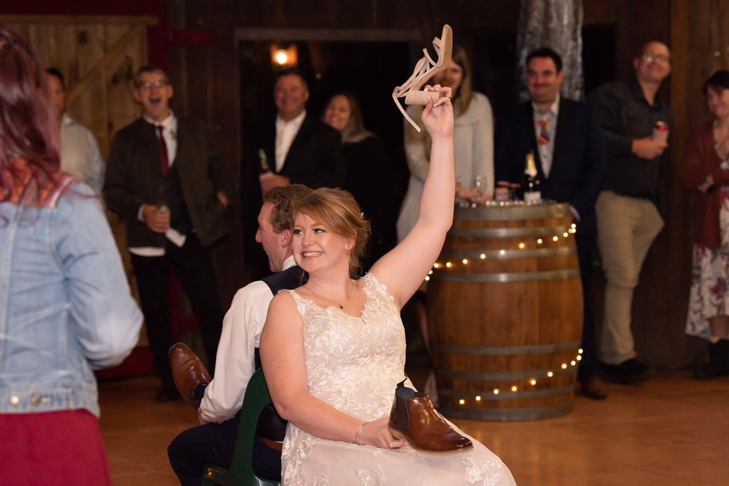 Dancer in a white lace dress raises their hand joyfully on the dance floor with wine barrels and lights in the background.