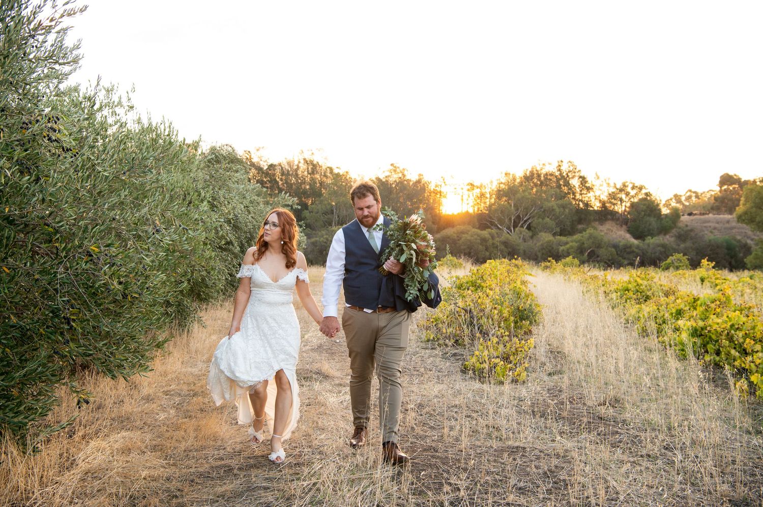 Couple walking through a golden sunset field during their wedding photoshoot.