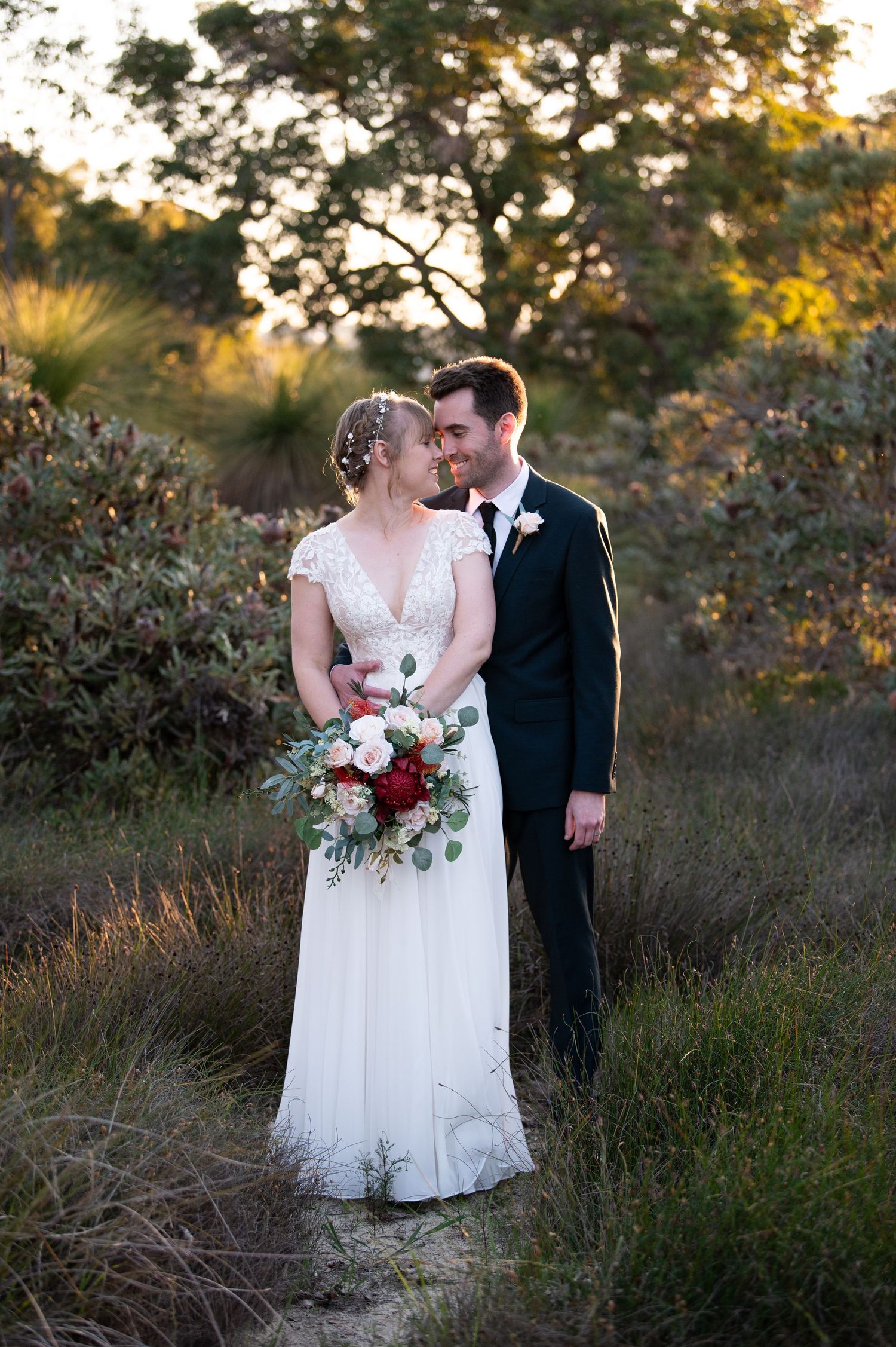 Romantic sunset wedding portrait in a natural outdoor setting with tall grass and autumn foliage.