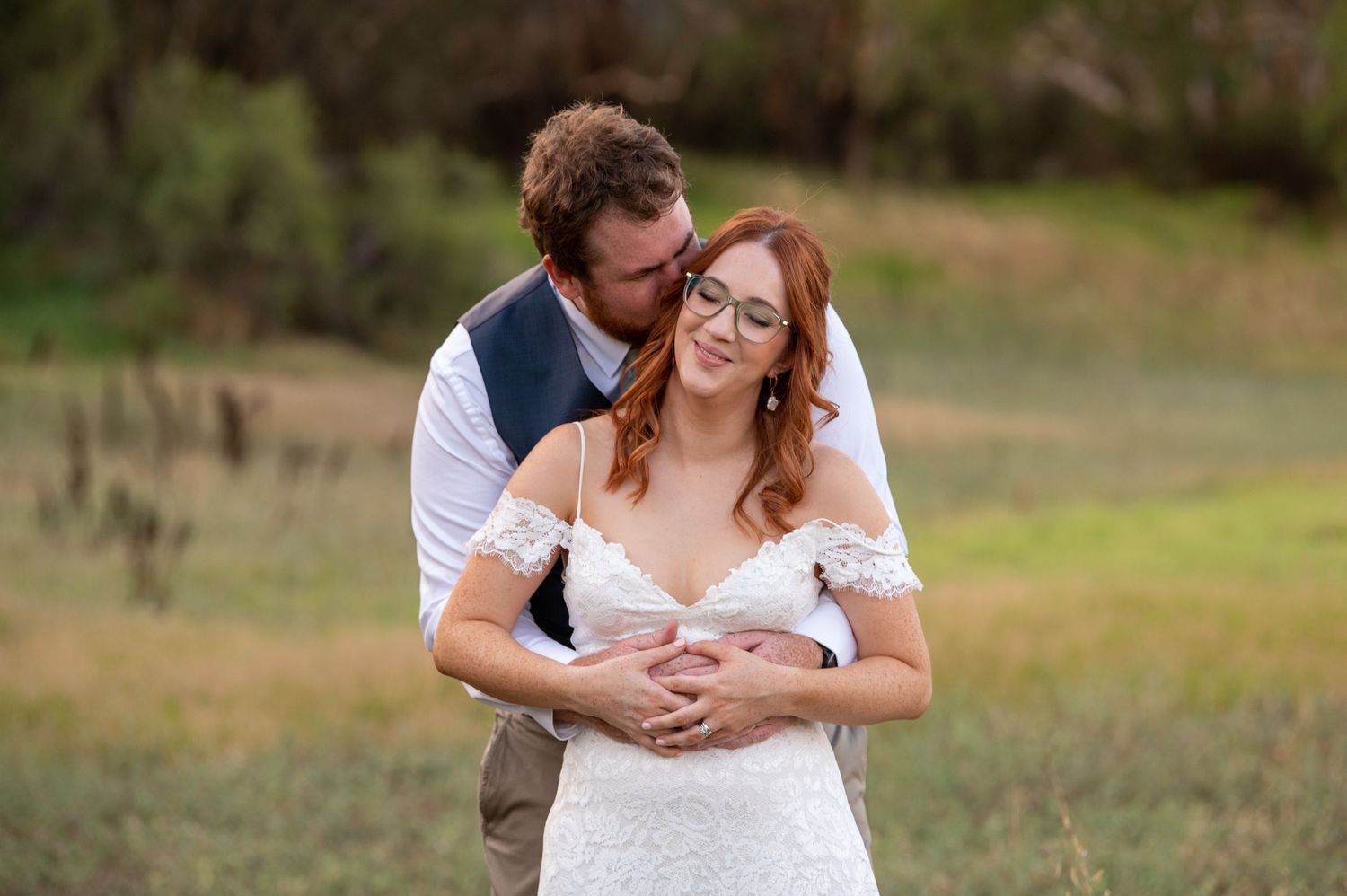 A couple embraces in a sunlit outdoor field during a wedding photo session.