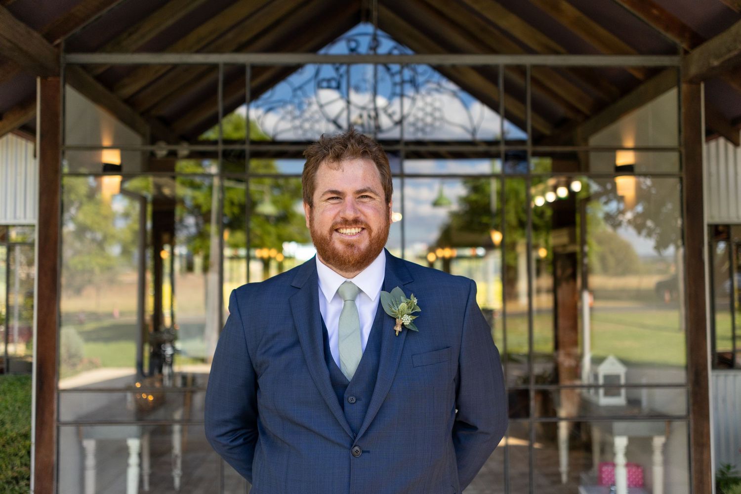 Groomsmen in navy suits gather under a rustic wooden pavilion.