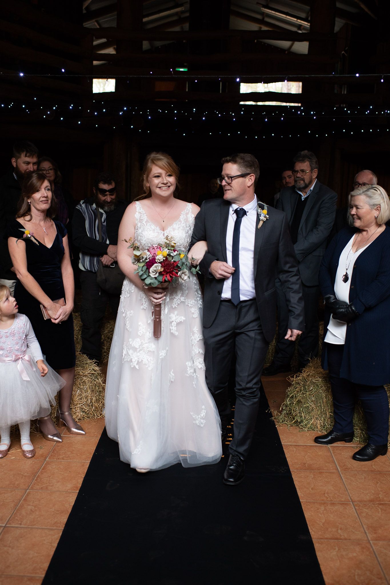 Wedding reception guests dancing and celebrating on a rustic dance floor decorated with string lights above.