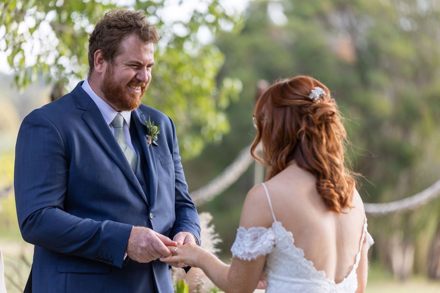 A tender moment during an outdoor wedding ceremony as a couple exchanges rings amongst garden greenery.