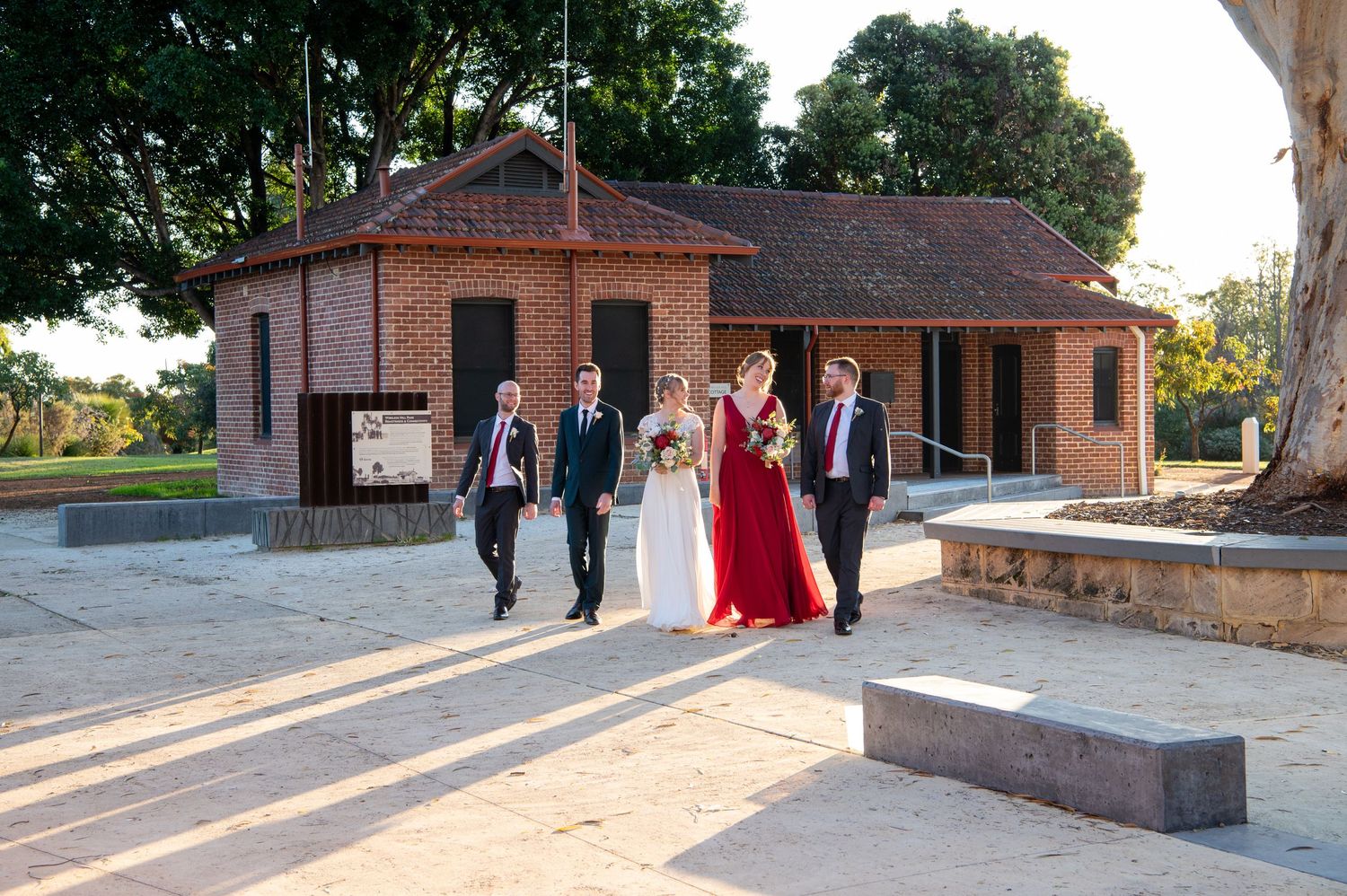 A wedding party walks outside a brick building during golden hour sunset.