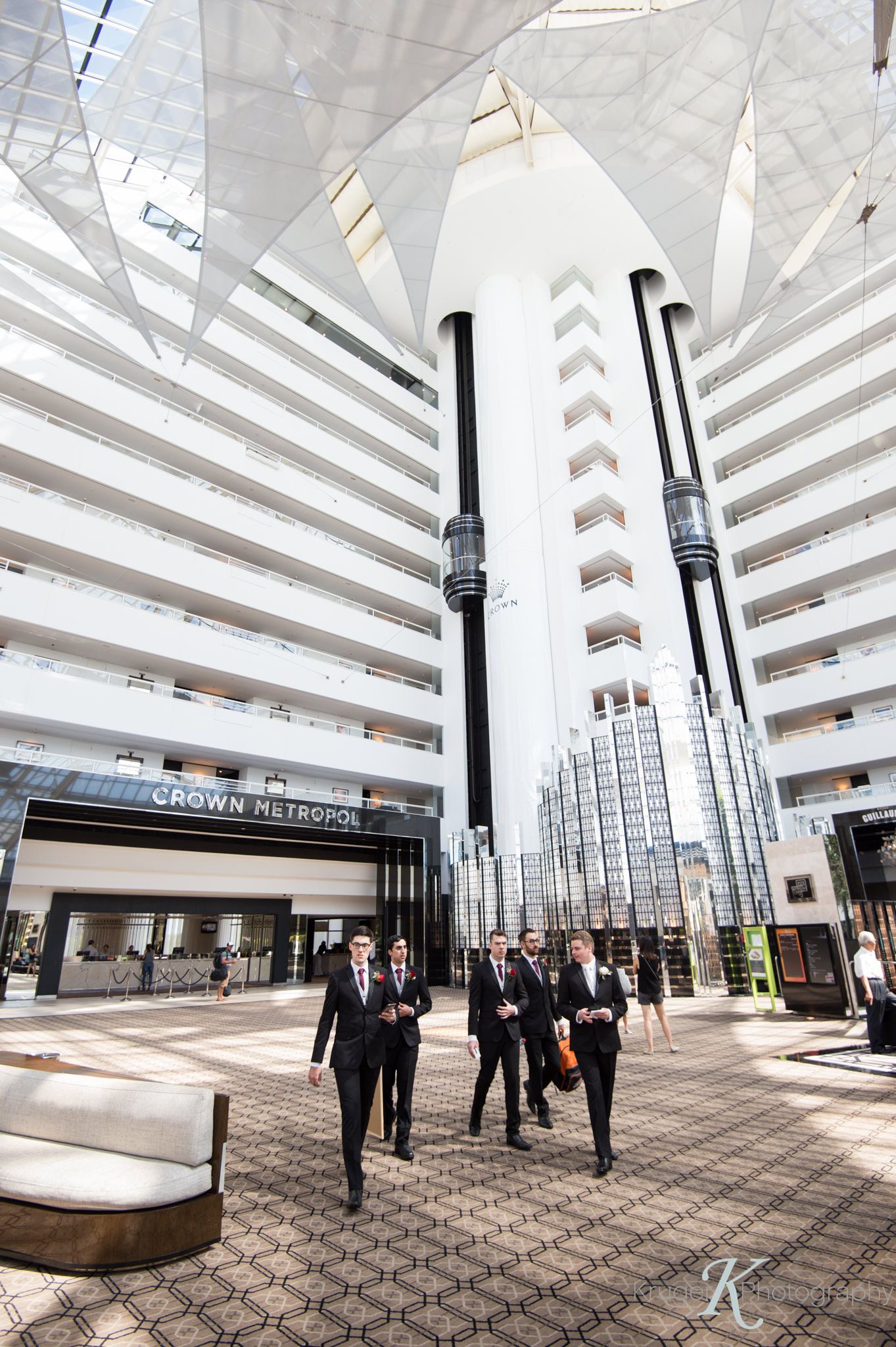 Groom and his groomsmen walk with purpose to their limousine through the lobby of Crown Metropol with geometric white architecture