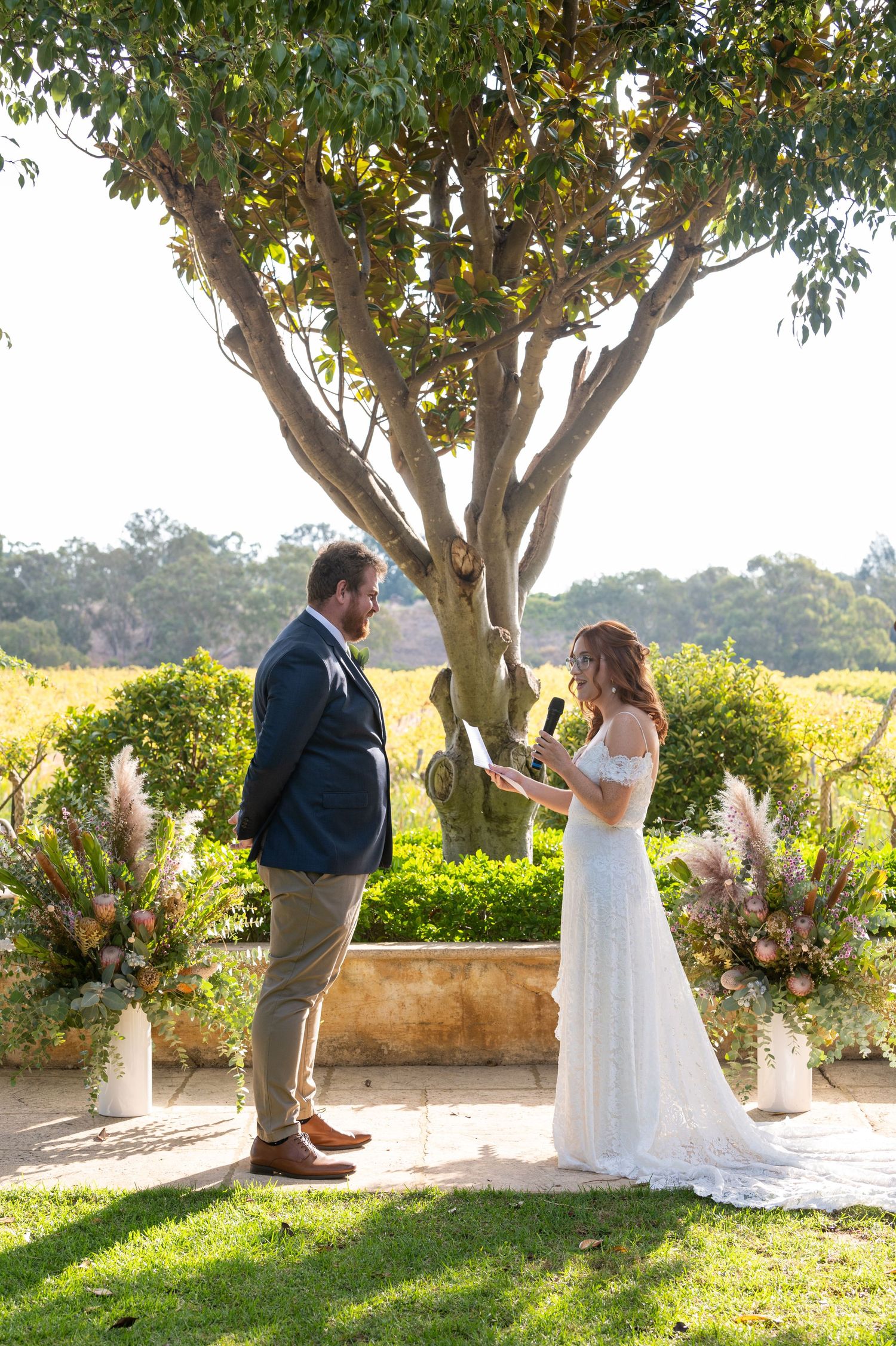 A romantic outdoor wedding photoshoot captures a couple in white and navy against a backdrop of trees in golden sunlight.
