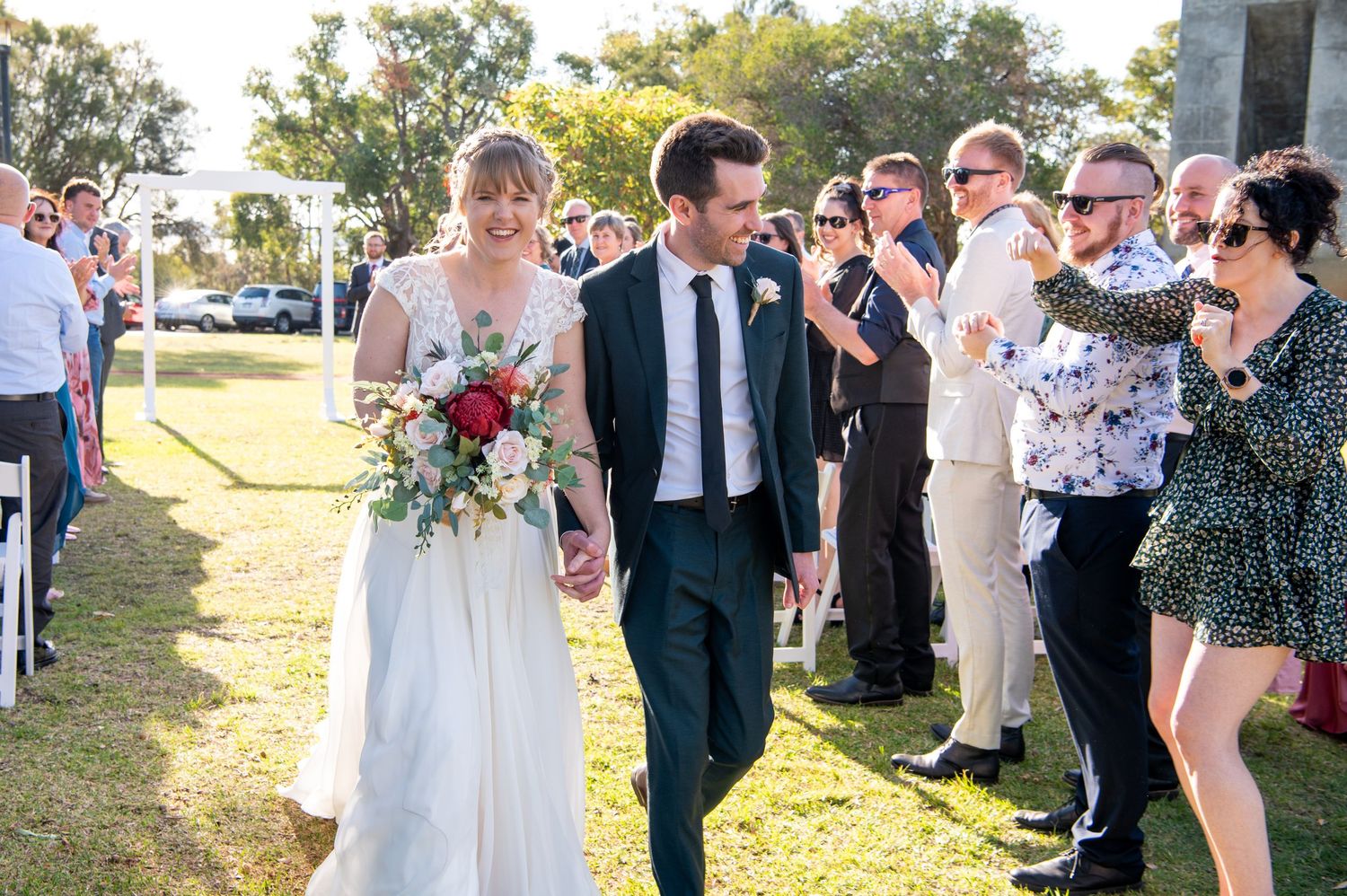 Newlyweds walk down the aisle while wedding guests celebrate their union outdoors.