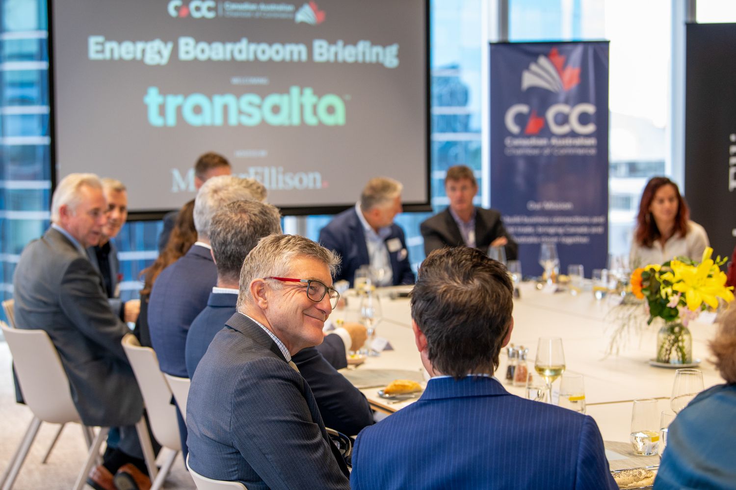 Business professionals gathered around tables at a corporate networking event with conference banners and displays in background.