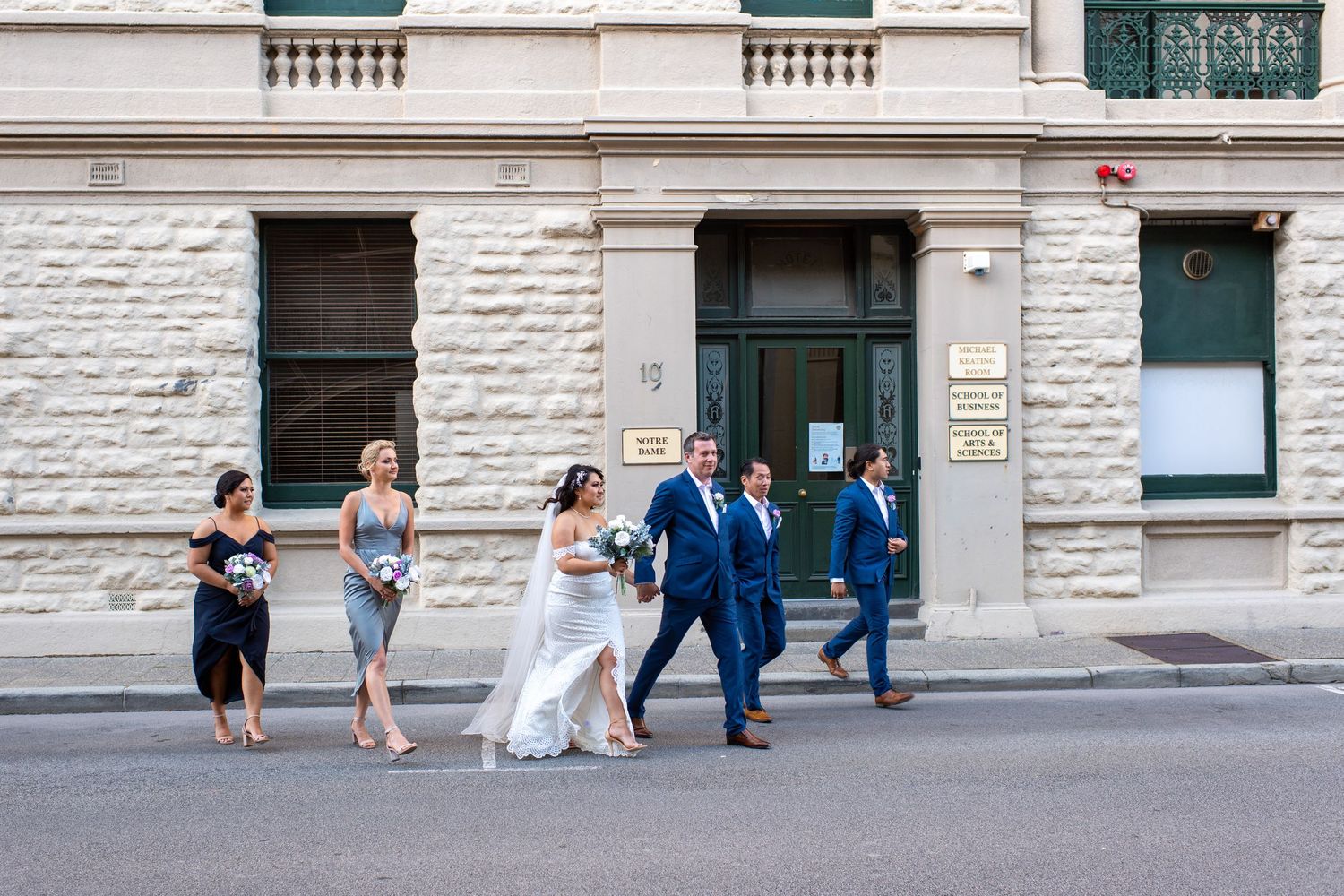 A wedding party strolls down a city street lined with classic stone buildings.
