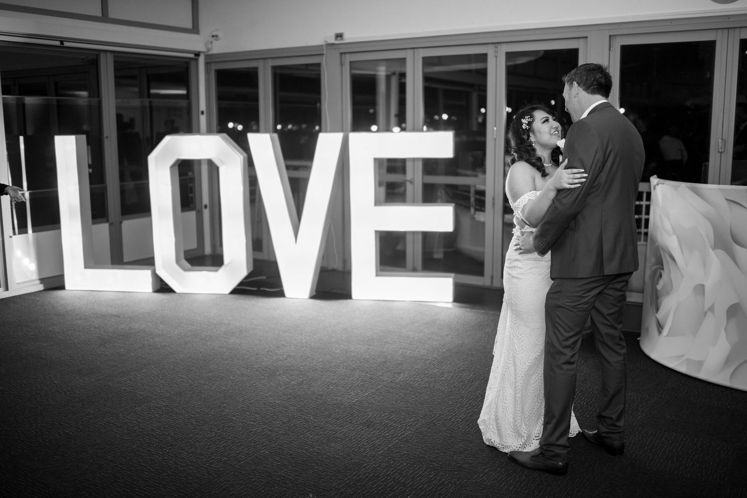 Couple sharing a romantic moment in front of large illuminated LOVE letters at an evening reception.