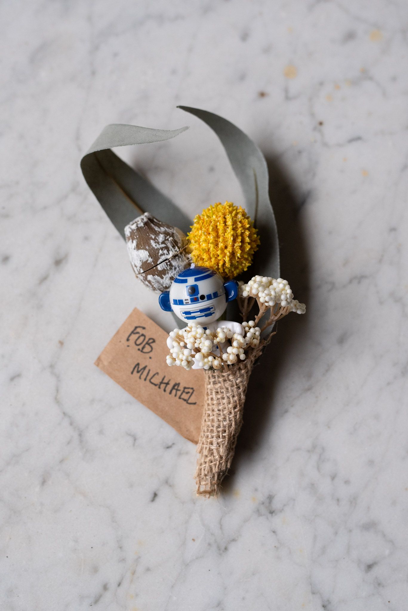 Star Wars inspired boutonniere with R2-D2 bead, yellow and metallic accents, and baby's breath wrapped in burlap.