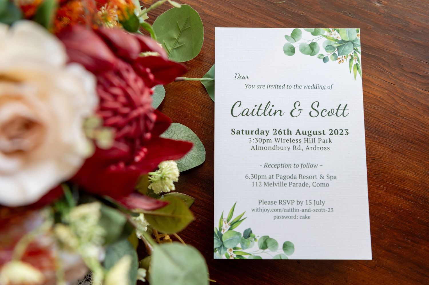 Wedding invitation suite featuring floral details and eucalyptus greenery on a wooden surface.