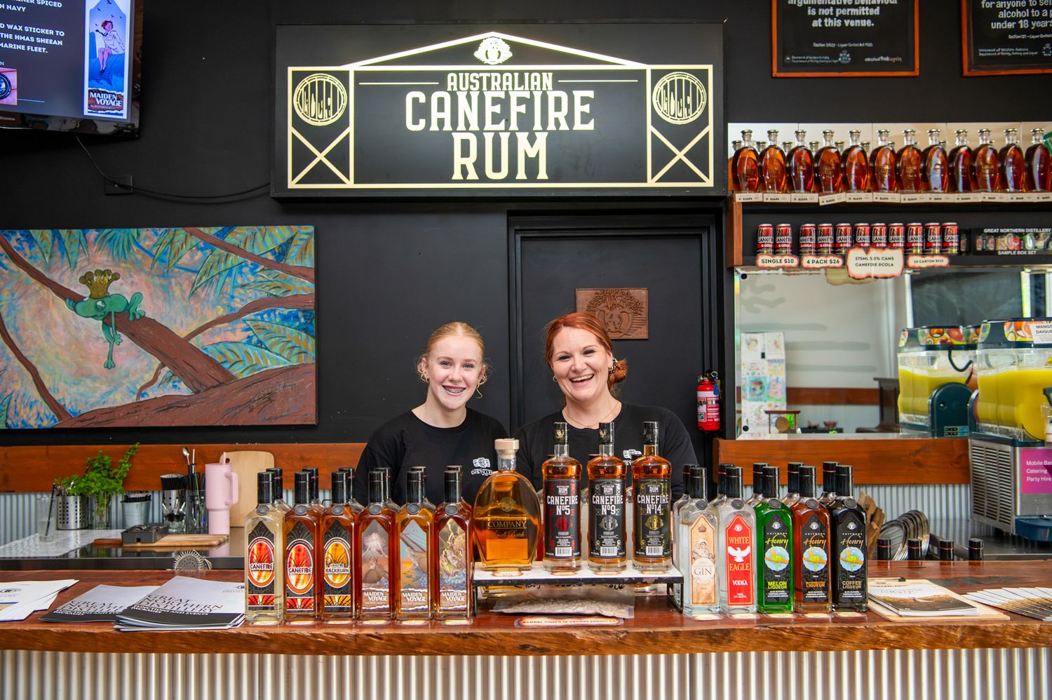 Bottles of craft spirits lined up on wooden bar shelves with decorative lighting and signage in the background.