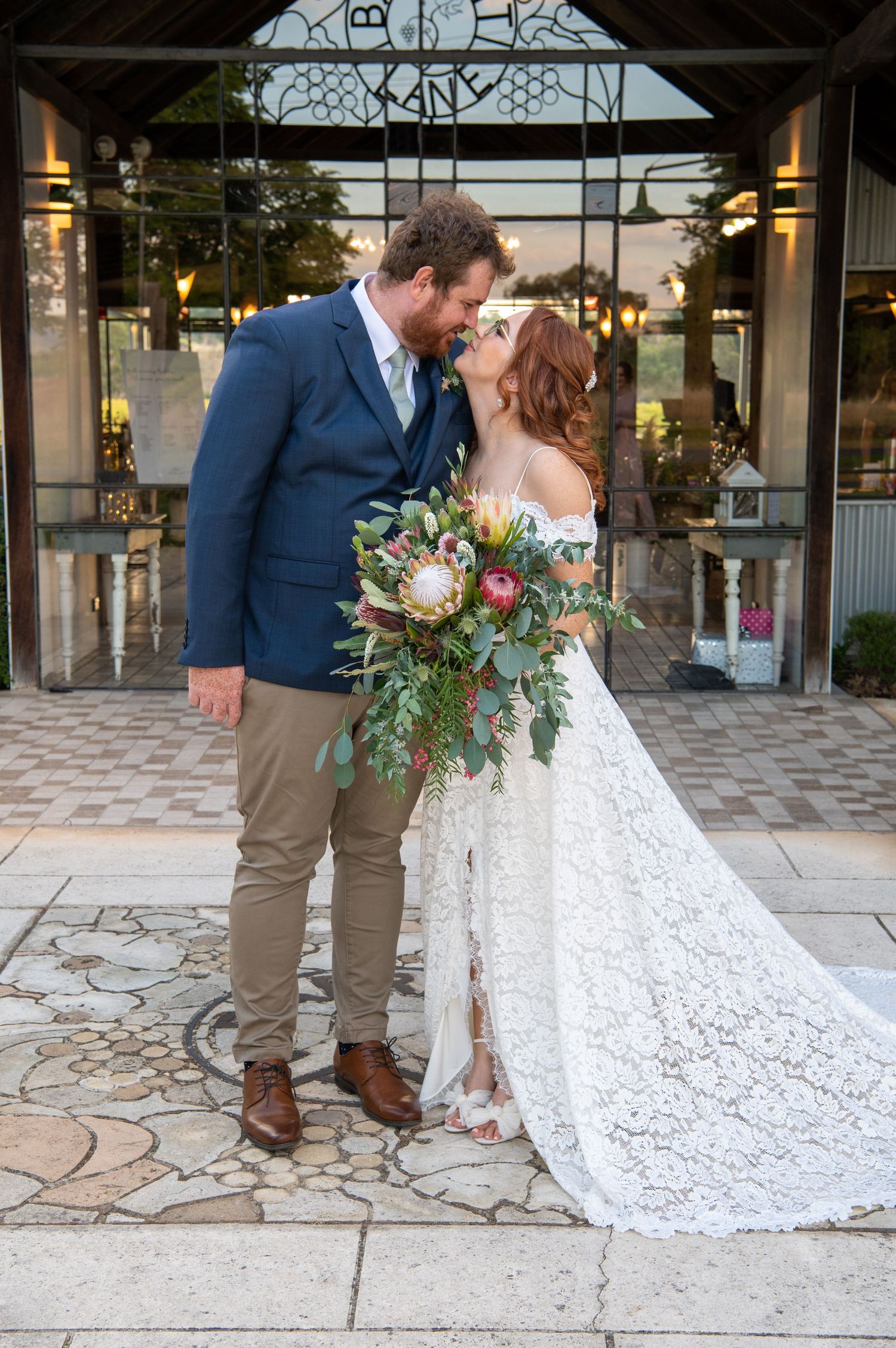 A couple in wedding attire posing on a stone patio under a covered walkway.