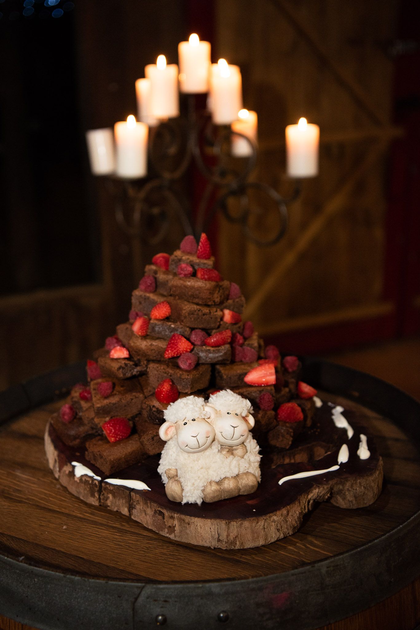 Dark chocolate meringue dessert with fresh raspberries and lit candles on rustic wooden board creates romantic atmosphere.