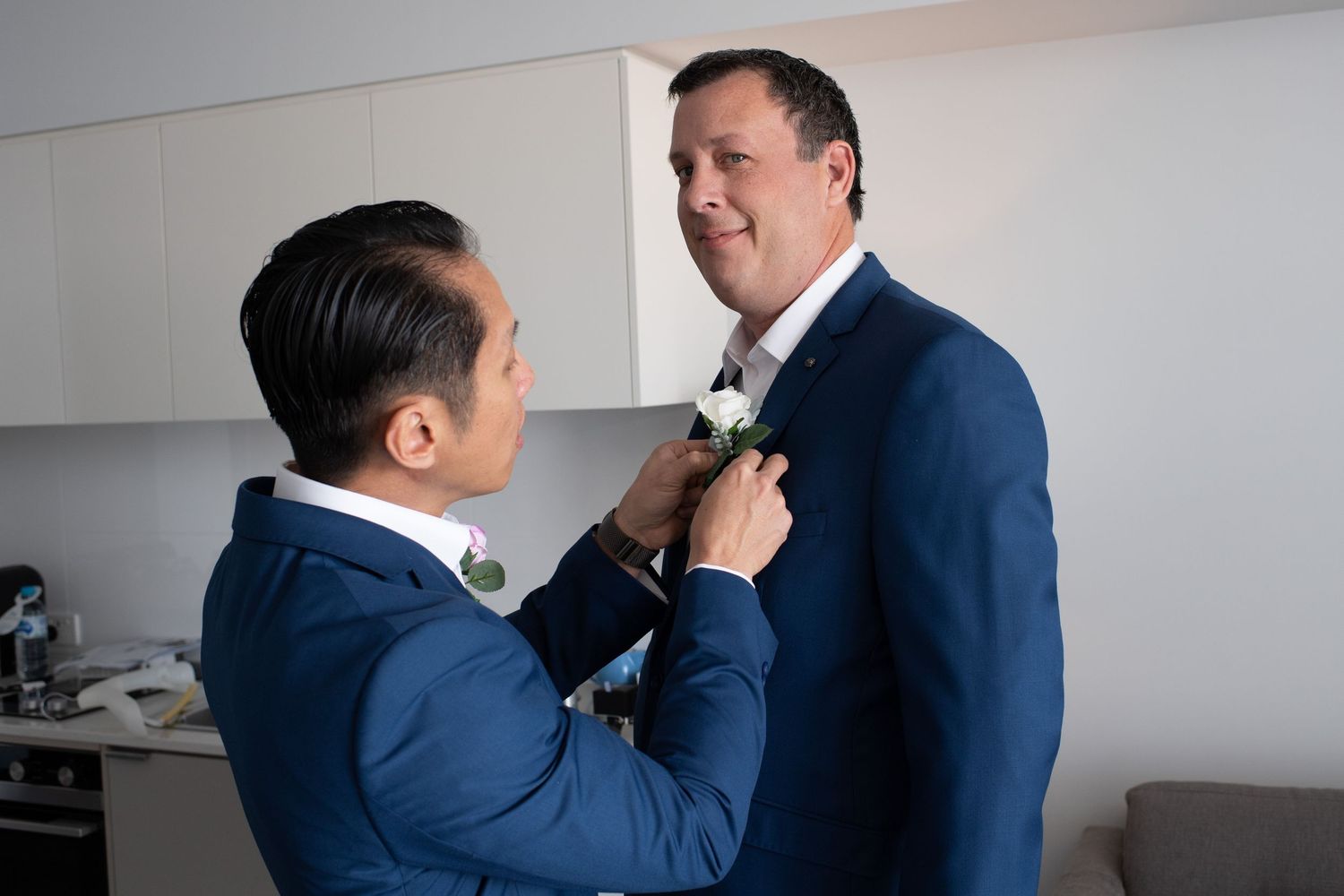 Two people in blue suits adjusting formal attire during preparation.