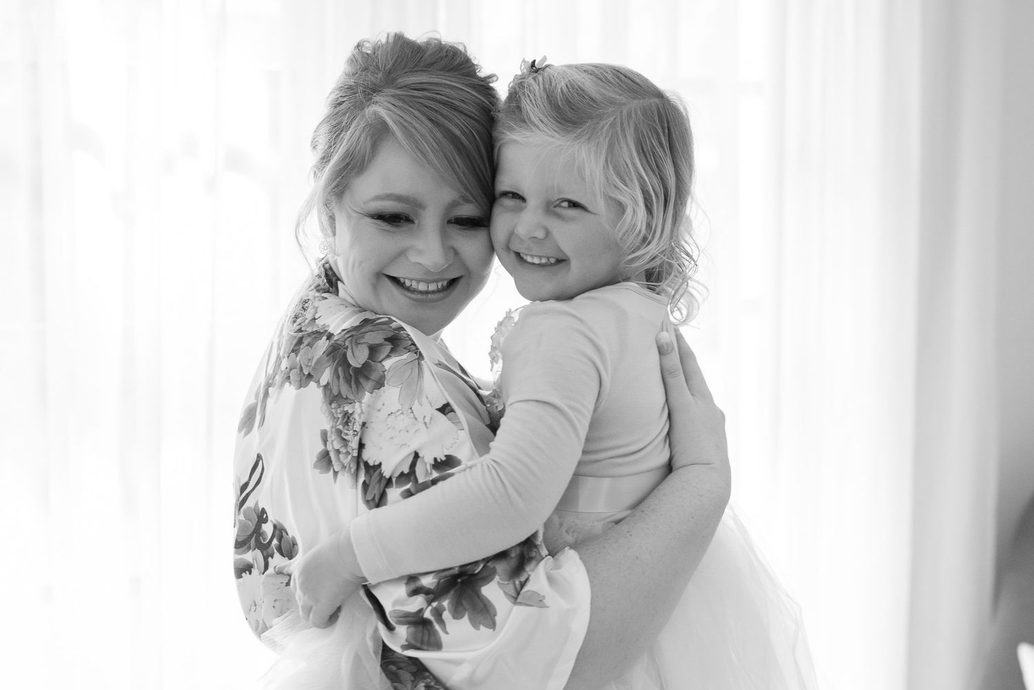 A parent in black holds a smiling young child wearing white, shown in a collage of black and white photos.