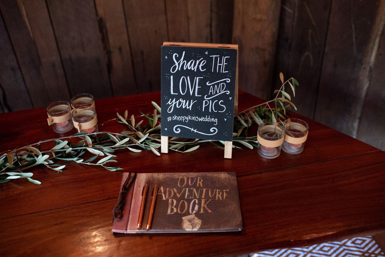 Wedding decor featuring a chalkboard sign, guest book, and small glass vases on a rustic wooden table.