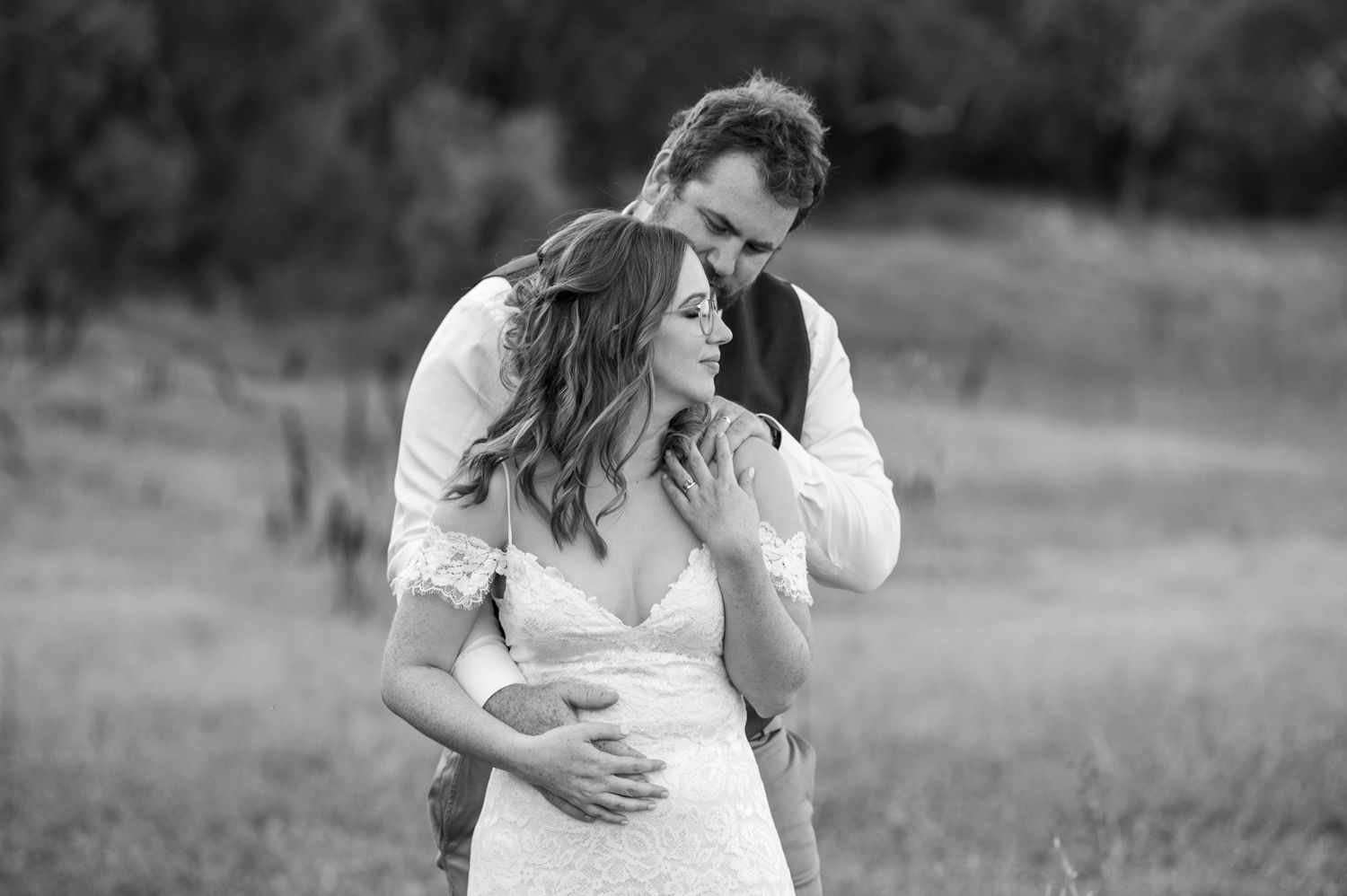Black and white photo of a couple embracing in a sunlit meadow during a romantic outdoor photoshoot at the venue Barrett Lane, Perth