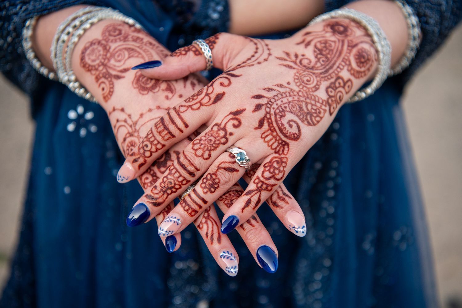 Intricate henna designs decorating hands holding each other against a dark blue background.