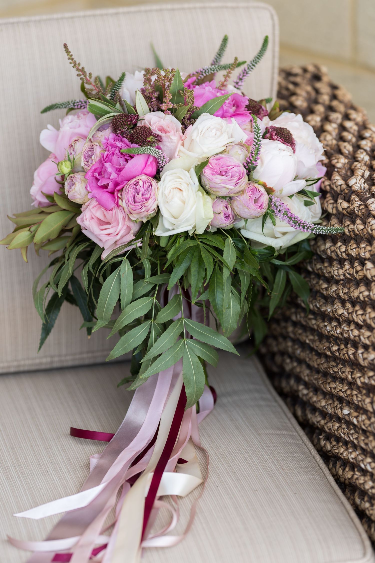 A romantic bridal bouquet with pink and white peonies, roses and greenery tied with flowing pink and burgundy ribbons.