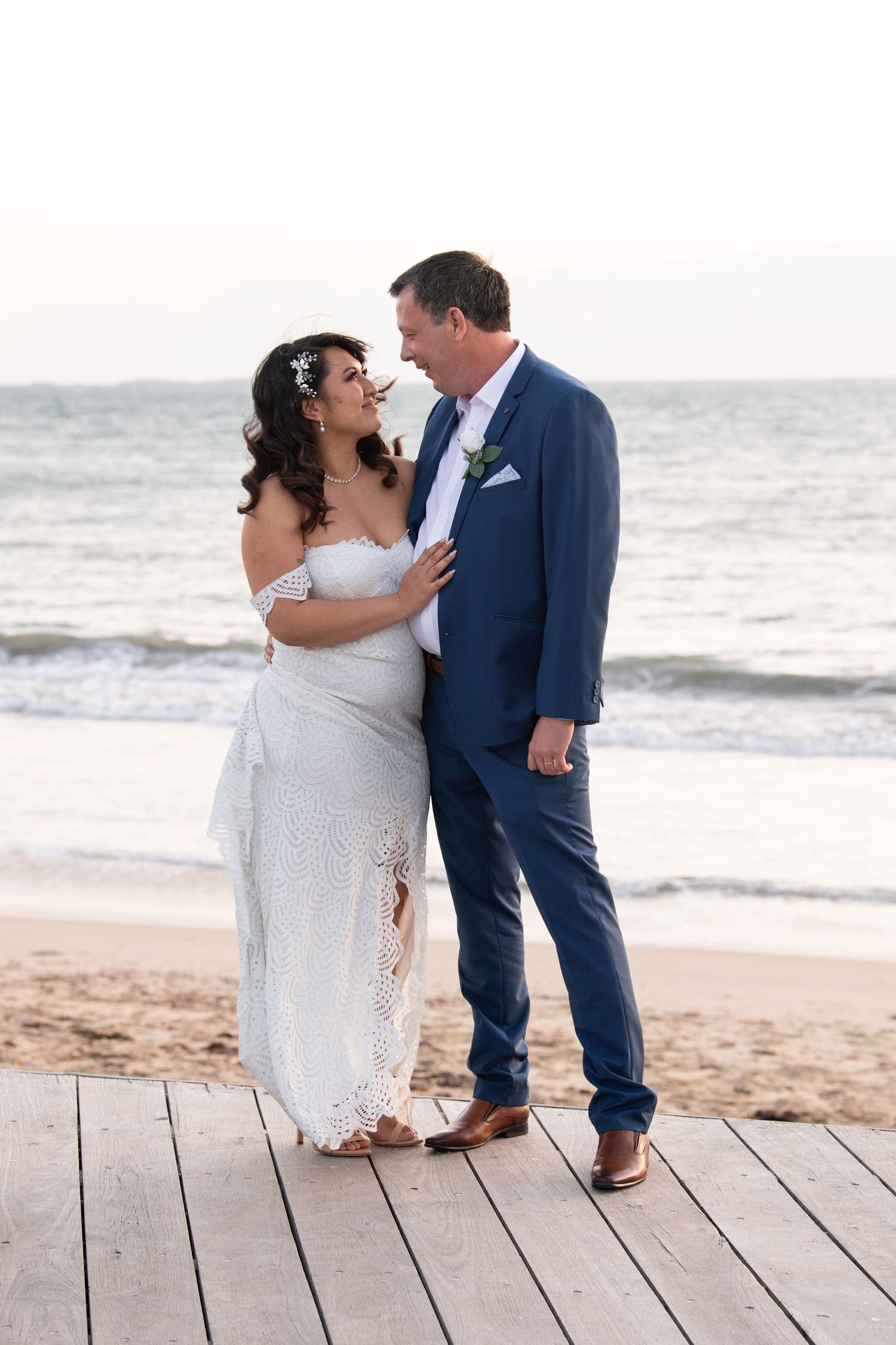 A romantic moment between newlyweds on a wooden boardwalk with the ocean waves in the background.