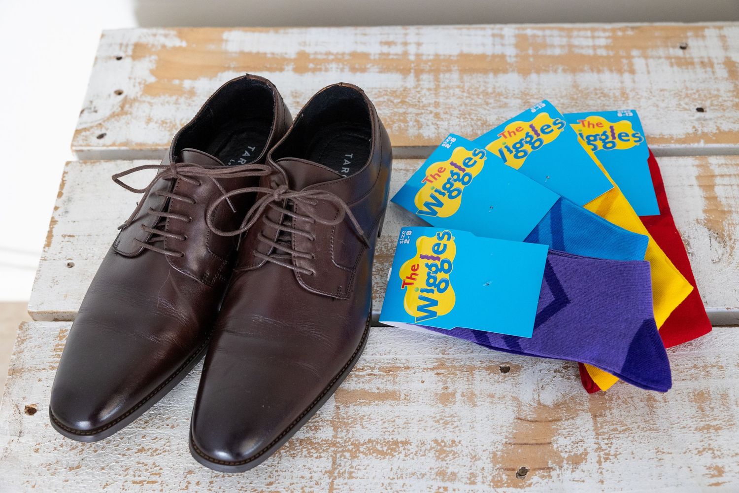 Brown leather dress shoes displayed next to colorful patterned socks on a rustic wooden surface.