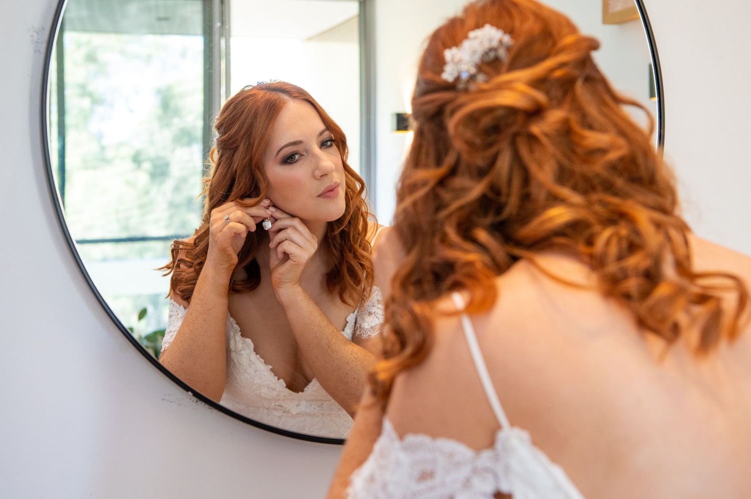 Elegant bride with curled hair and vintage styling getting ready in front of a circular mirror.