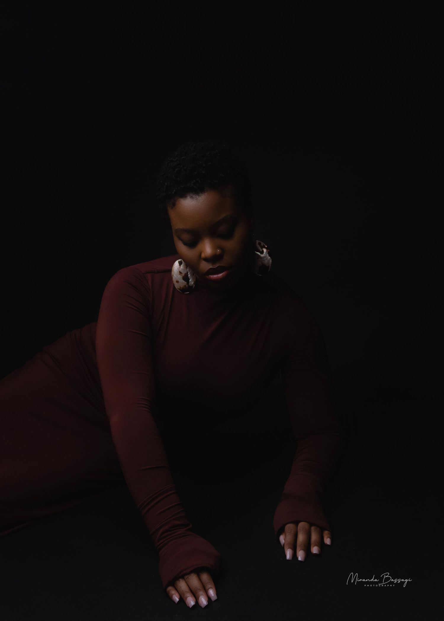 Dramatic low-key portrait in burgundy sweater against black background.