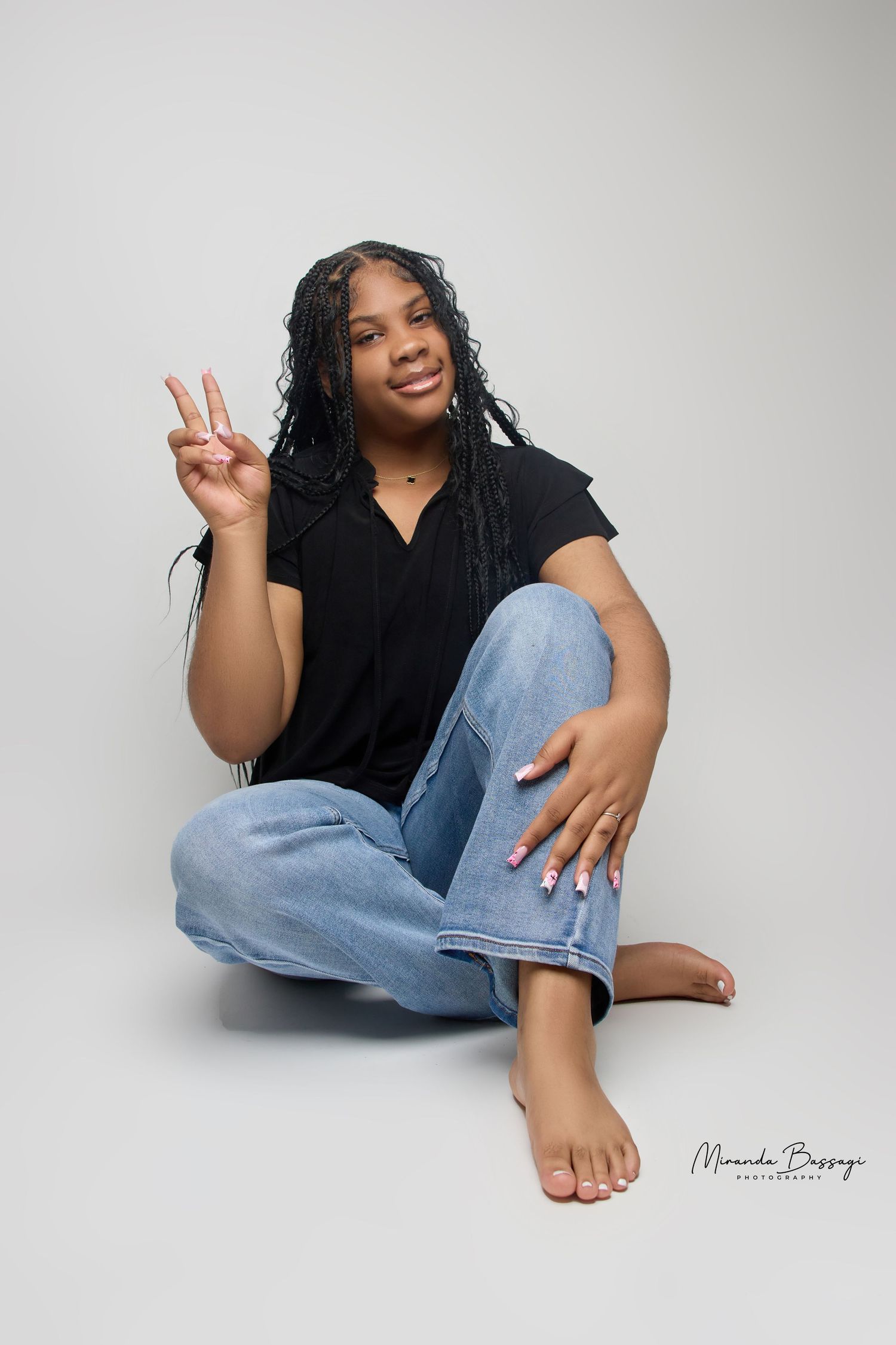 Model in black shirt and jeans poses casually on white studio floor.