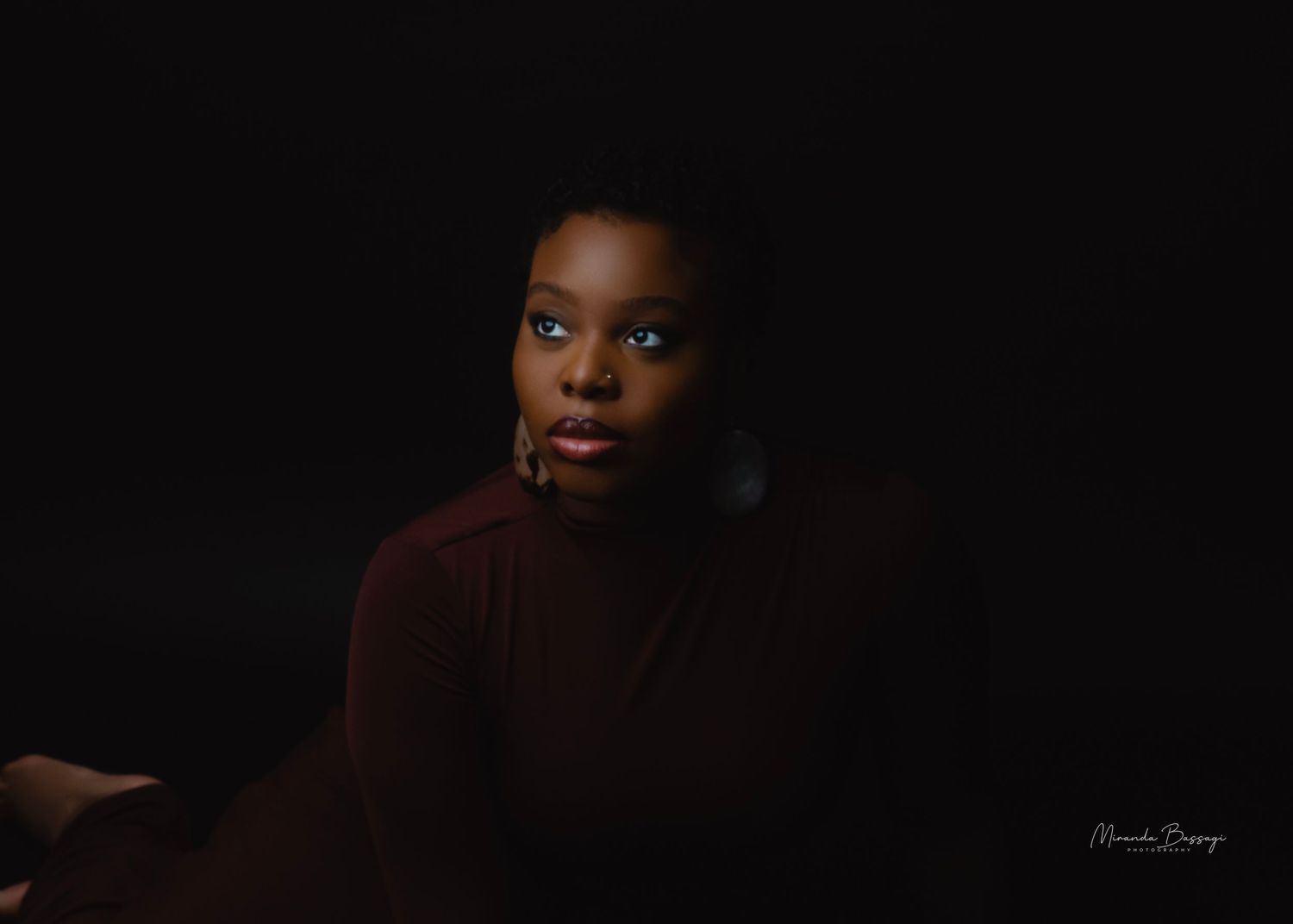 Low-key portrait in burgundy turtleneck against black background with dramatic lighting.