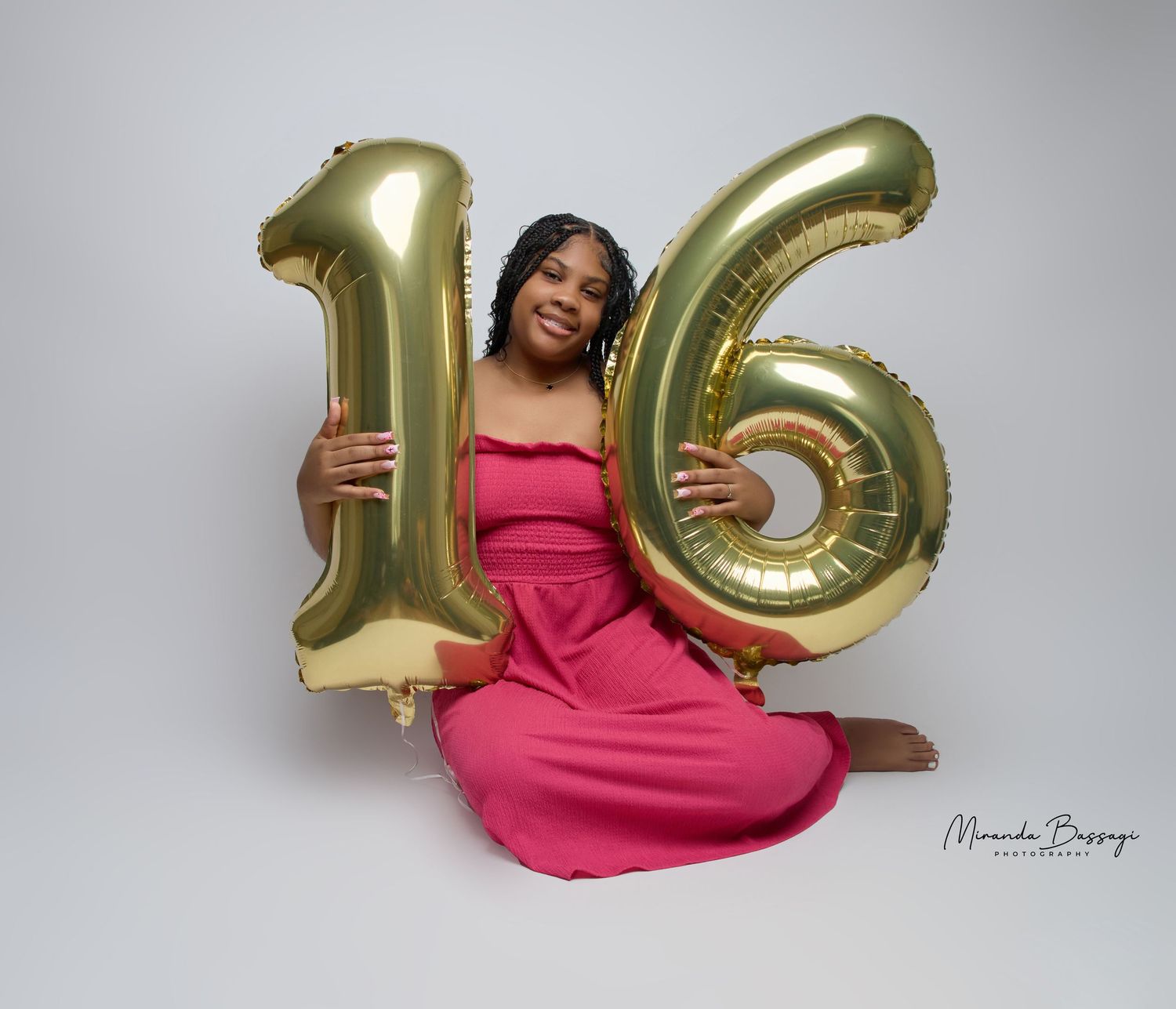 Model poses with gold '16' balloons wearing pink dress in studio setting.