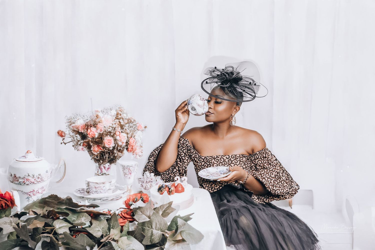 Elegant tea party setup with pink roses and a person in an off-shoulder dress posing near a vintage teapot.
