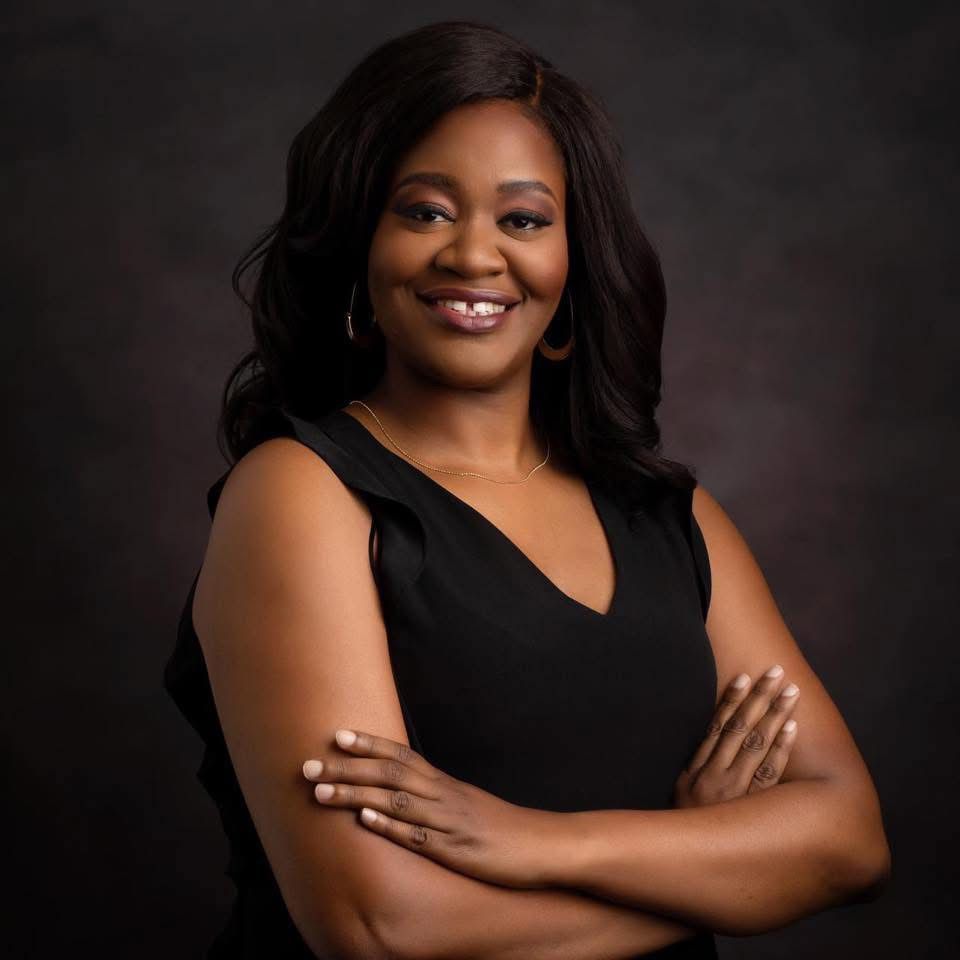 Professional studio portrait with person in black v-neck dress against dark background.