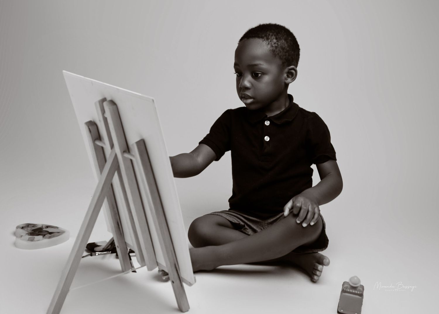 Black and white minimalist portraits of toddler with chair against light background.