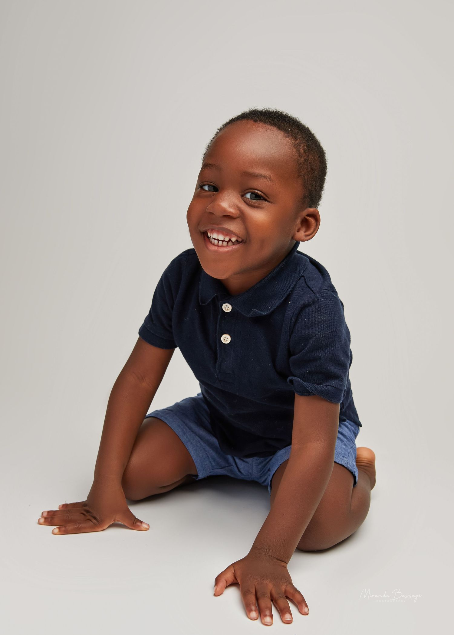 Playful studio portraits of young child in navy polo shirt against white background.